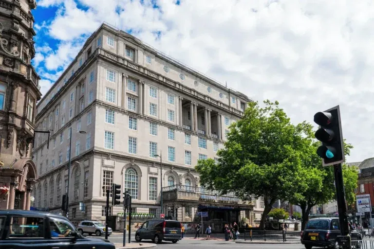Large pale stone Adelphi Hotel Edwardian hotel building on a Liverpool city centre corner, with tall windows, a central colonnade and a leafy tree beside the street