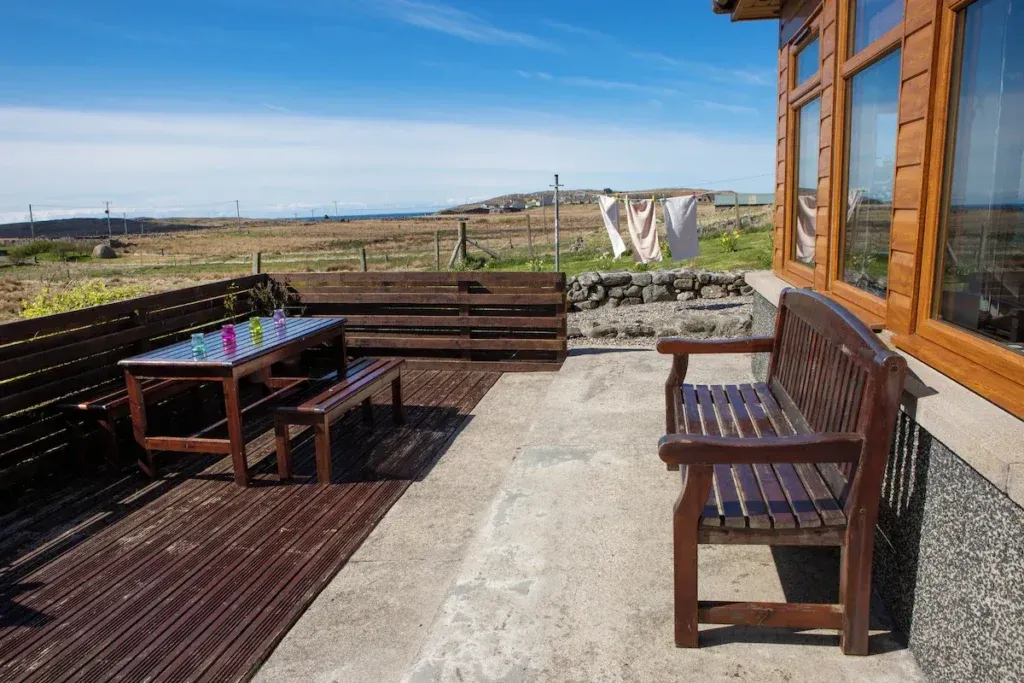 Wooden picnic table and bench outside An Taigh Clach with views across crofting land towards the sea