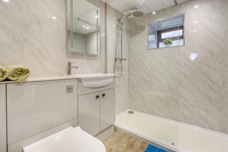 Bathroom with marble-effect wall panels, a large shower with a glass screen, a white vanity unit with basin and an illuminated mirror