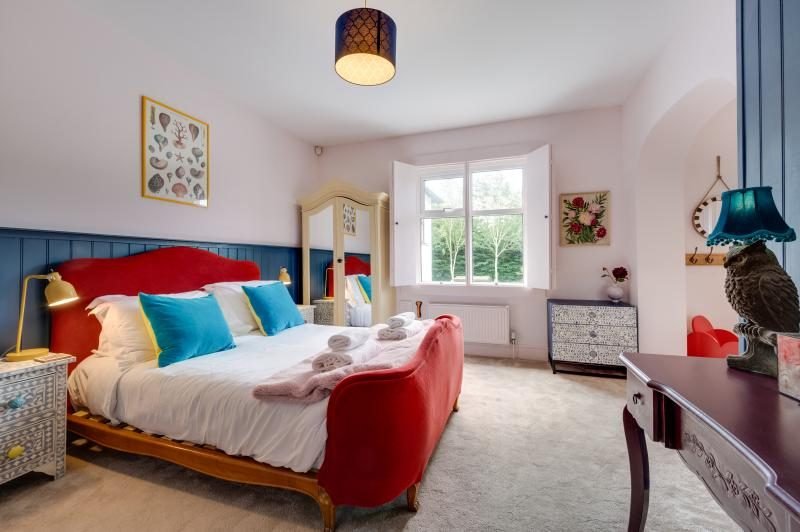 Colourful Cinema House near Craster, Northumberland 13 Bedroom with red velvet bed, teal cushions, blue panelling and a mirrored wardrobe