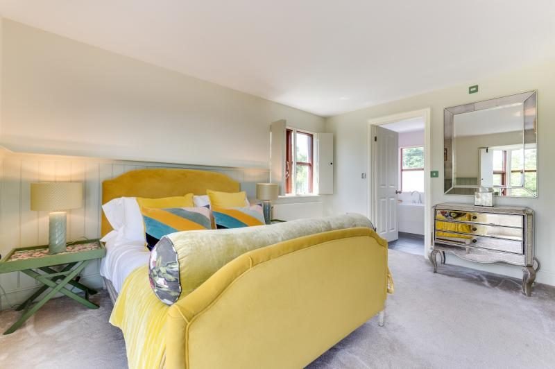 Colourful Cinema House near Craster, Northumberland 11 Bedroom with yellow velvet bed, mirrored chest of drawers and a doorway to an en-suite
