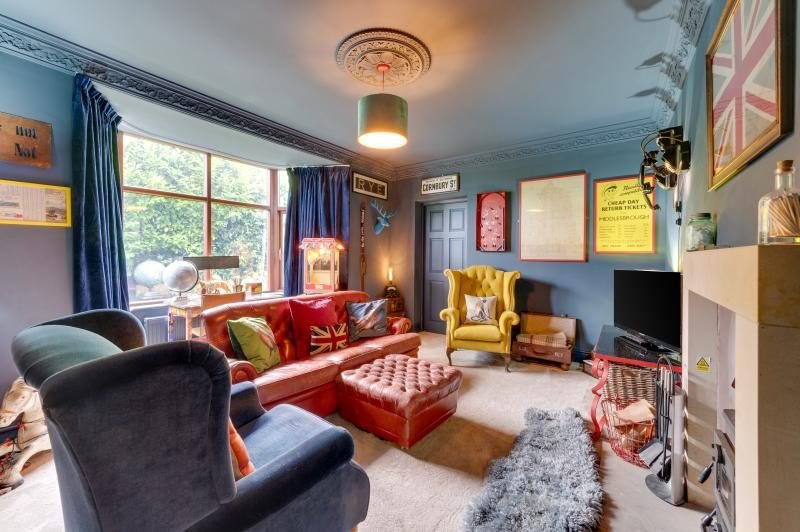 Colourful Cinema House near Craster, Northumberland 9 Blue sitting room with tan leather sofa, yellow armchair, bay window and ornate cornicing