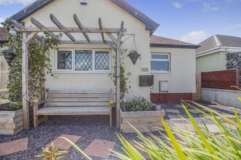 Bungalow exterior with a wooden arbour and bench, raised planters and a gravelled front garden