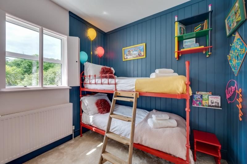 Colourful Cinema House near Craster, Northumberland 14 Blue panelled bedroom with red metal bunk beds, a wooden ladder and colourful shelves