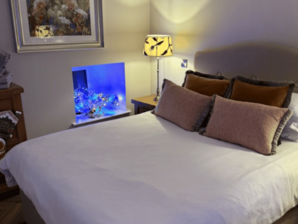 Double bed with layered cushions beside a bedside lamp and blue illuminated wall alcove at Cabra Cottage