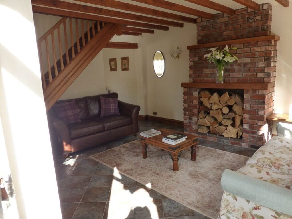 Lounge with exposed timber beams, two sofas, an internal staircase and a brick chimney breast at Cherry Tree Cottage