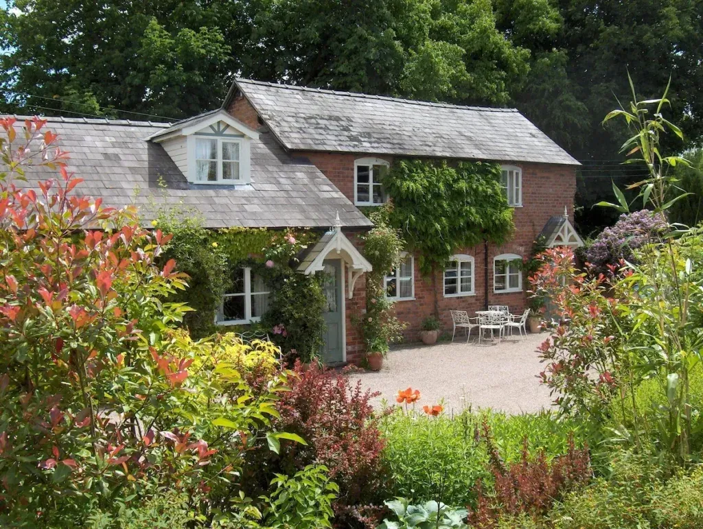 Brick cottages surrounded by mature garden planting with outdoor tables and chairs in Tarvin Sands at Cherry Tree Cottage
