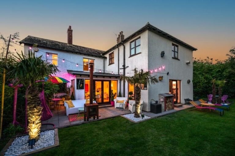 Rendered house at dusk with lit windows, string lights, palm trees and a lawn garden