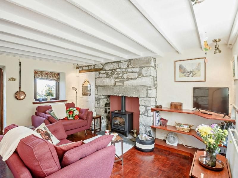 Cottage lounge with burgundy sofas, exposed ceiling beams, parquet flooring and a stone fireplace