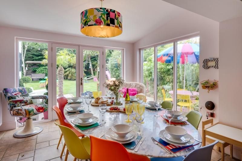 Colourful Cinema House near Craster, Northumberland 6 Round dining table laid for a meal with bright chairs and glass doors opening to the garden