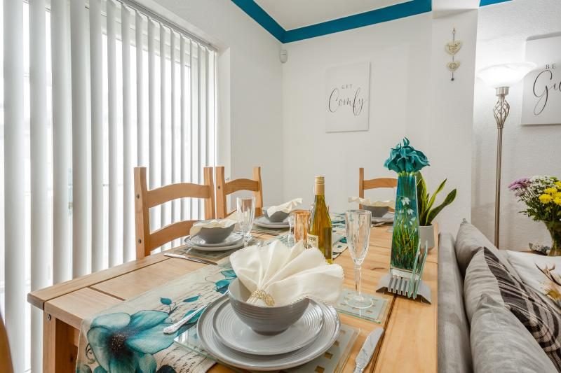Coastal Bungalow with Decked Garden, Kinmel Bay, North Wales 4 Pine dining table laid with grey bowls, glasses and napkins beside a grey sofa