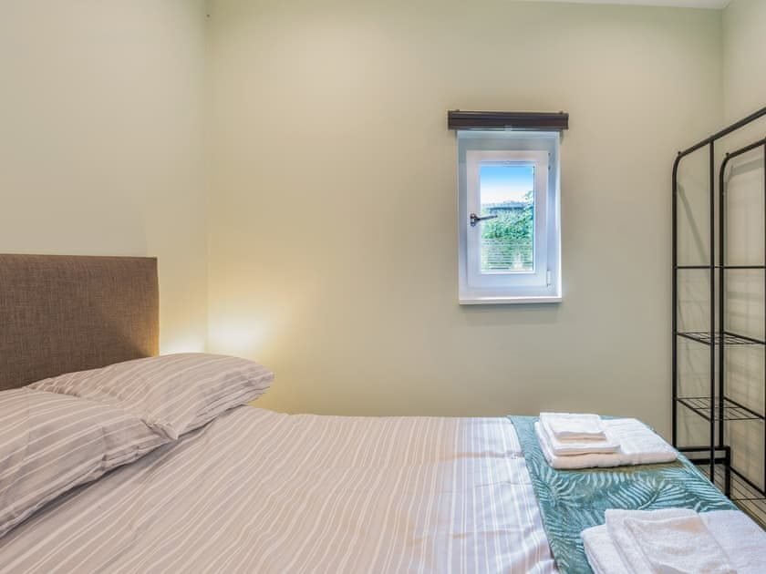 Double bed with striped bedding, upholstered headboard and folded towels beside a small window