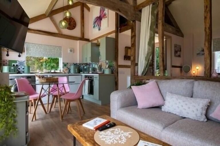 Open plan living area at Field View Cottage with exposed timber beams, sofa, kitchen and dining table