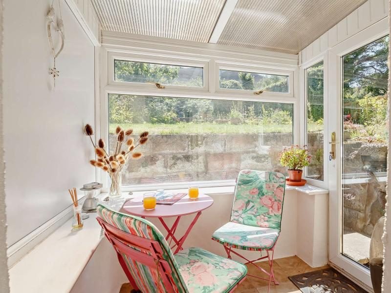 Glazed rear porch with a small pink table, floral folding chairs and views towards the garden
