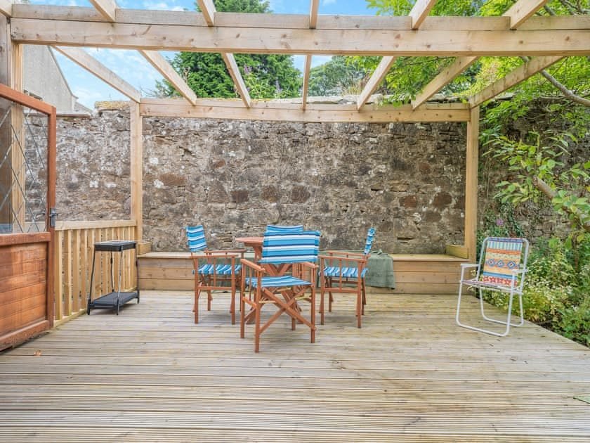 Gravel area with a timber store, stone pillar and an octagonal timber summerhouse with leaded windows, with a pergola deck behind