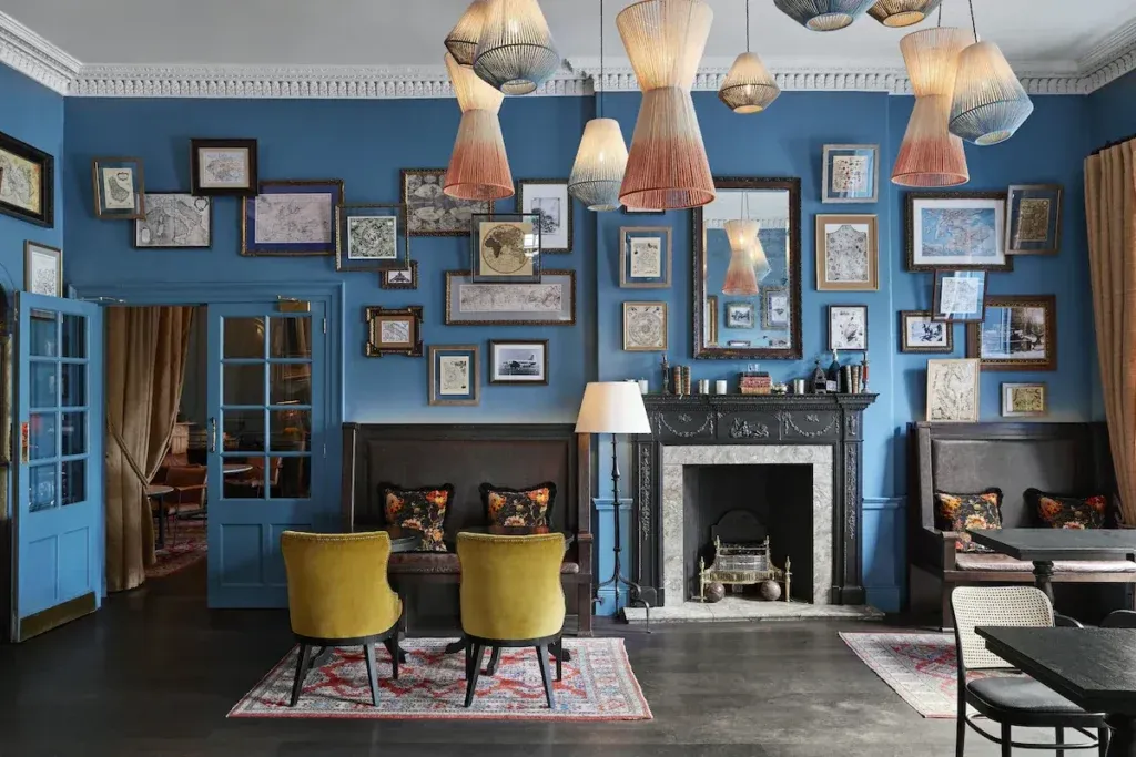 Blue lounge with framed maps, pendant lights, booth seating and a decorative fireplace at Kimpton Charlotte Square