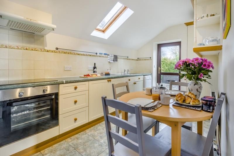 Kitchen with cream cabinets, electric oven and hob, a skylight, and a round wooden dining table set with breakfast pastries