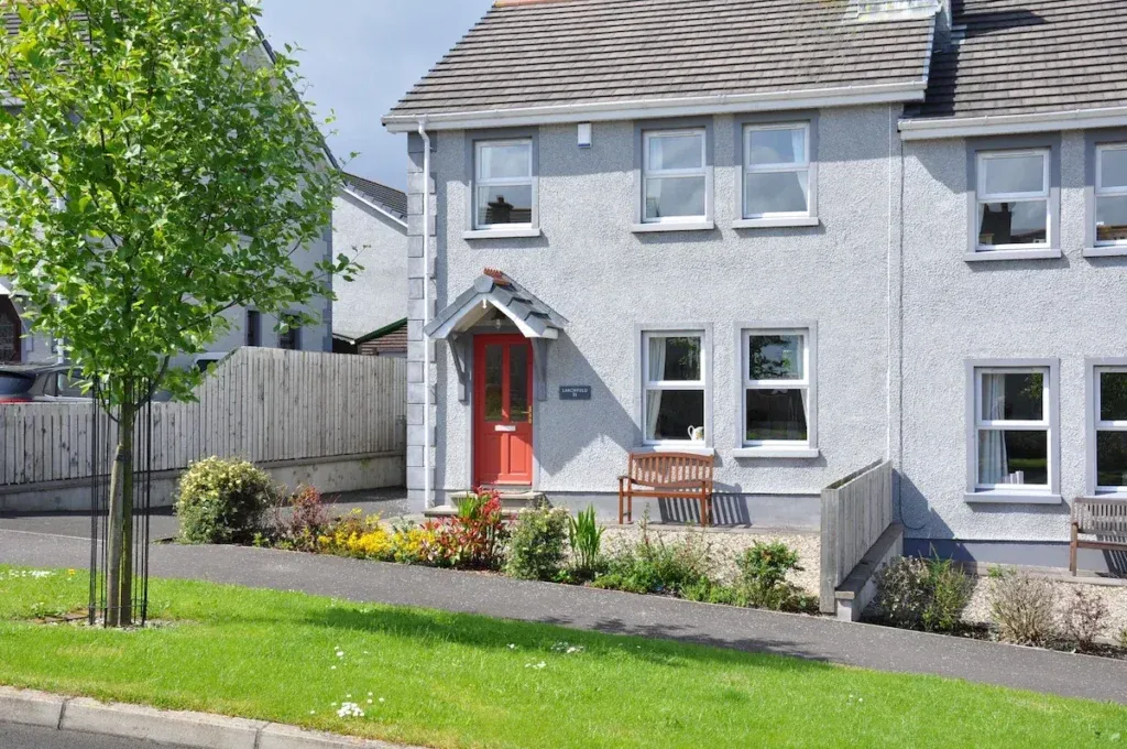Exterior of Larchfield holiday home in Bushmills with grey walls, red front door and landscaped front garden