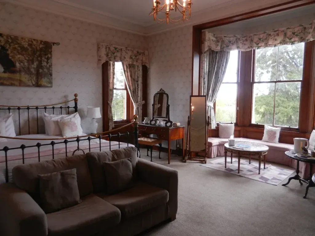 Bedroom with a metal bed frame, sofa, dressing table and seating beside a large bay window