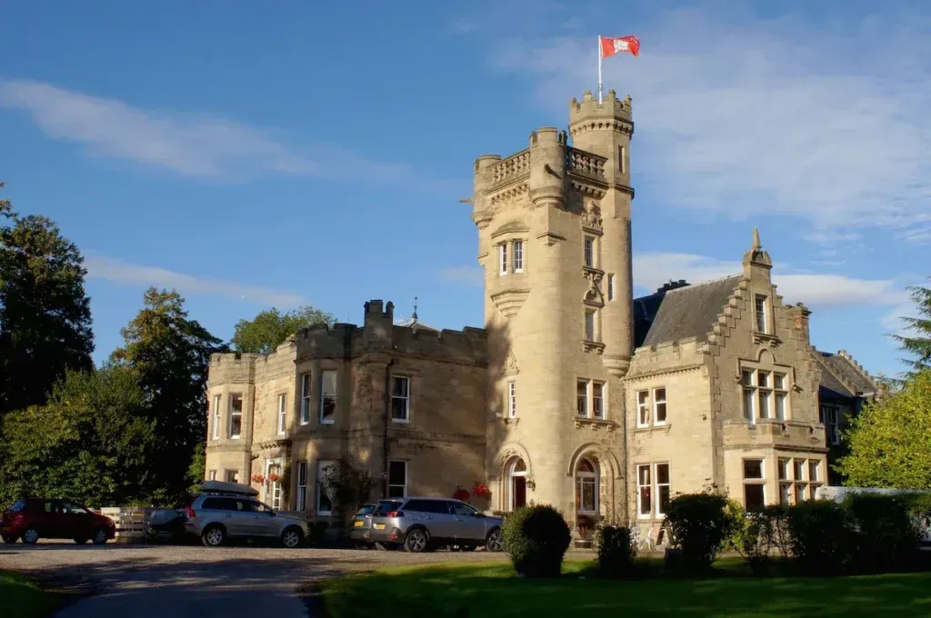 Stone exterior of Mansfield Castle Hotel with a tall turreted tower, arched entrance and lawn