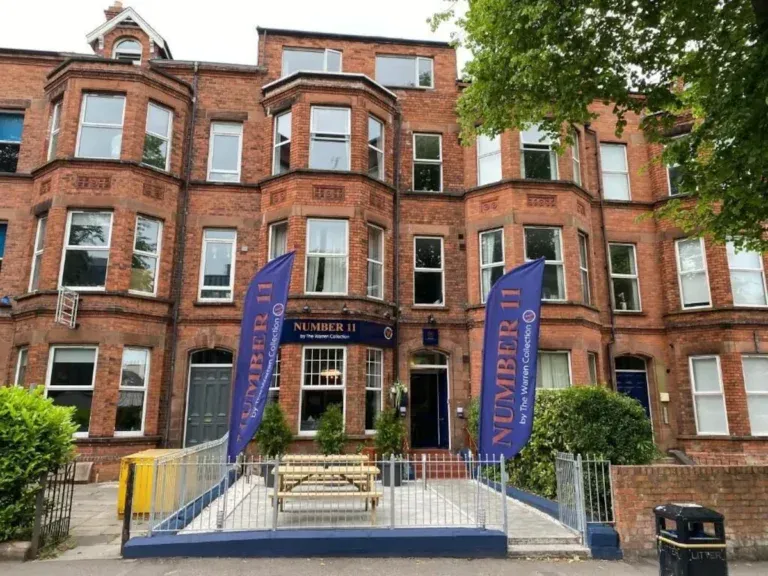 Red brick terraced hotel on Malone Road Belfast with blue Number 11 flags and outdoor picnic bench at the front