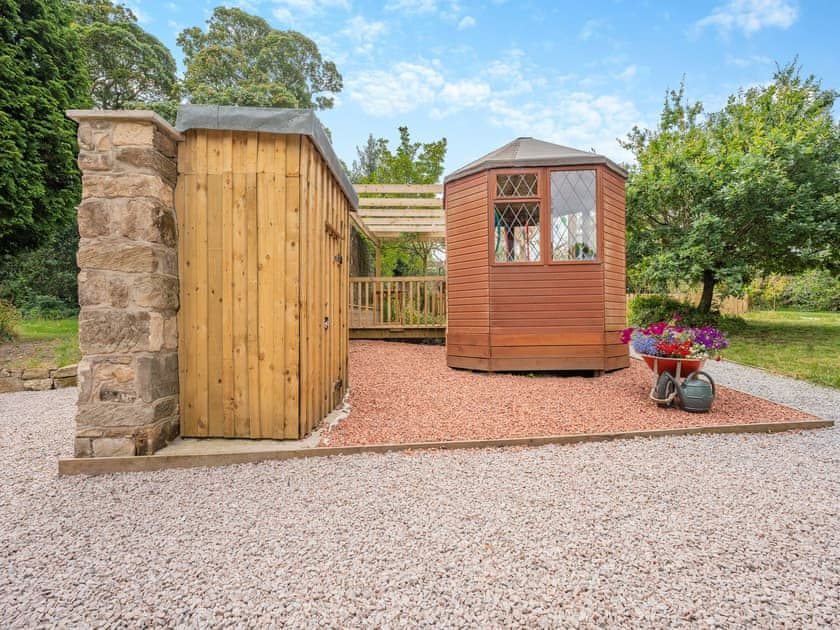 Timber pergola over a decked seating area with a table and chairs beside an old stone wall