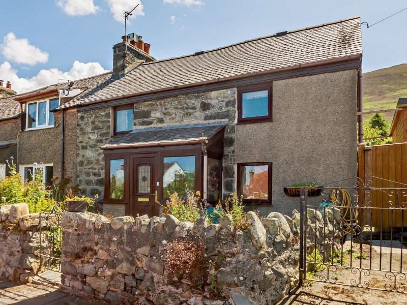 Stone and rendered cottage with an entrance porch, low stone wall and hillside behind