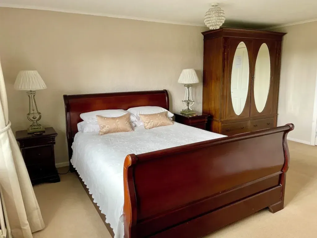 Wooden sleigh bed with white bedding, bedside lamps and a mirrored wardrobe