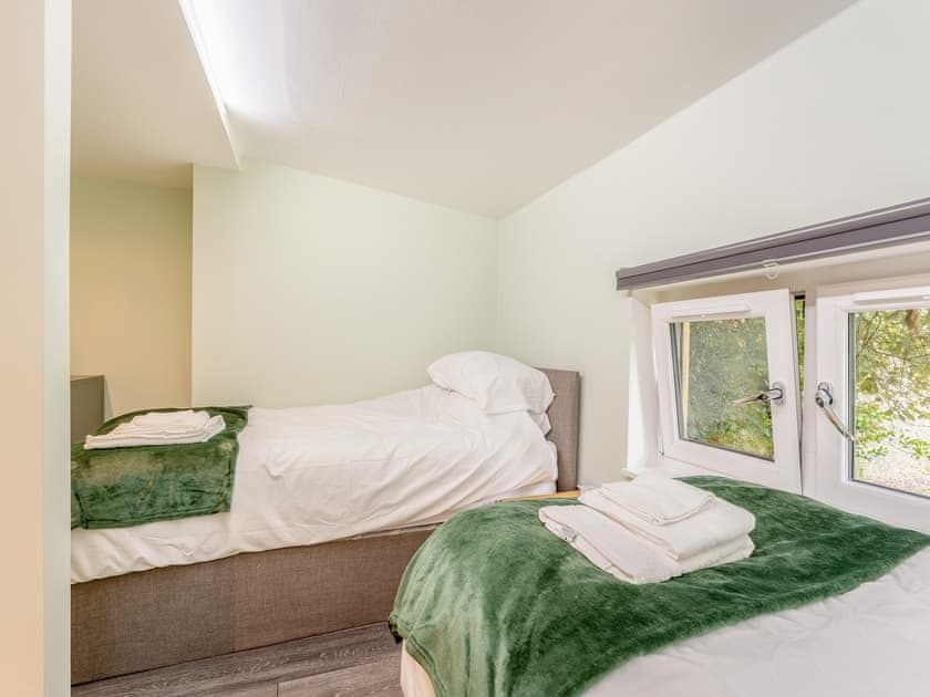 Two single beds with white bedding and green fleece throws under a sloping ceiling with windows overlooking trees