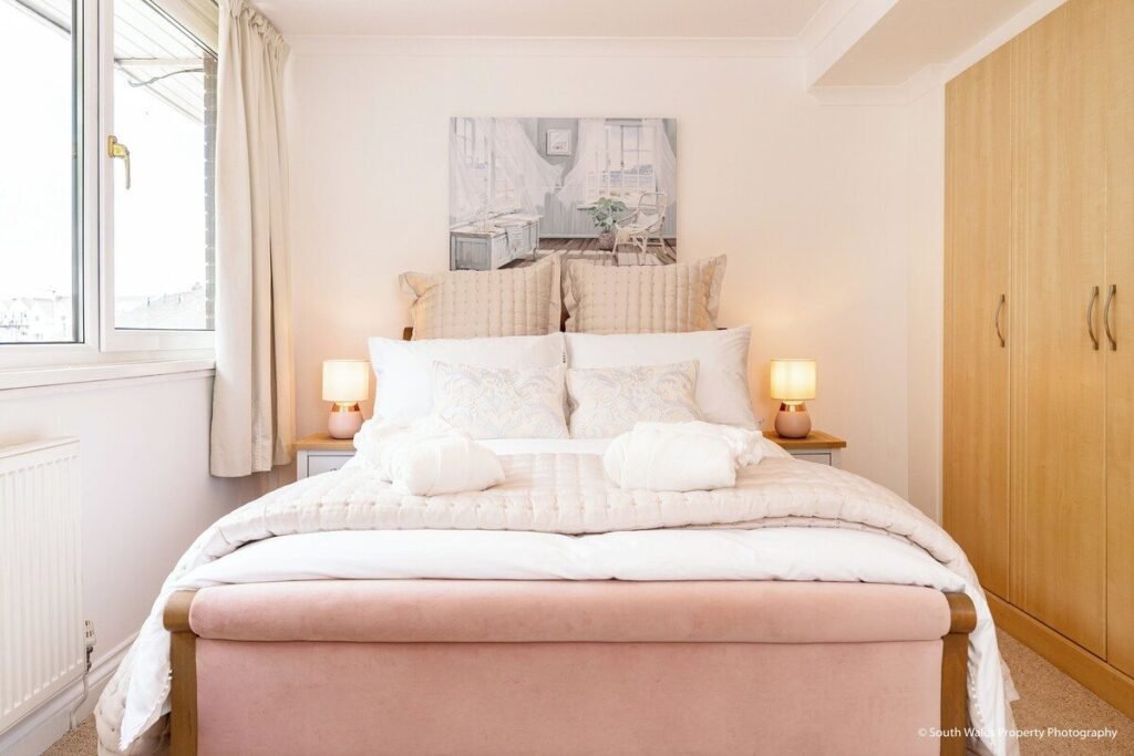 Bedroom with white bedding, a pink upholstered bed frame, bedside lamps and wooden wardrobes