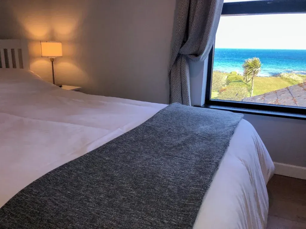 Double bed with white bedding beside a window overlooking the garden and Irish Sea at Seal Bay Cottage