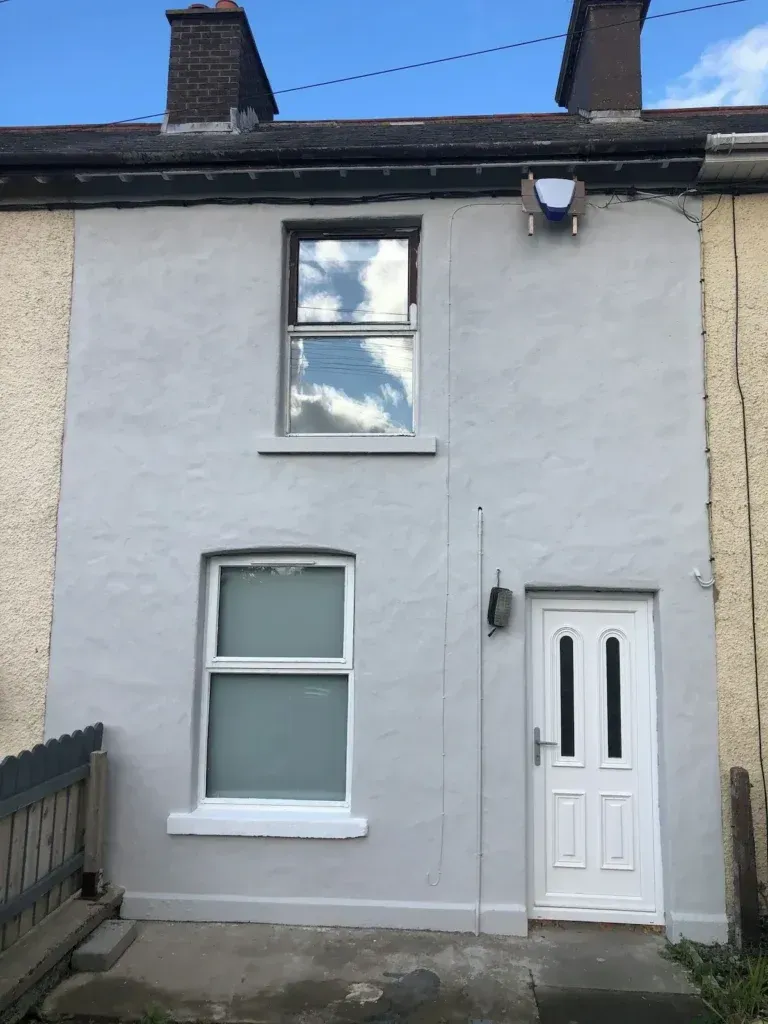 Front of Seal Bay Cottage with a white entrance door, two windows and chimney stacks
