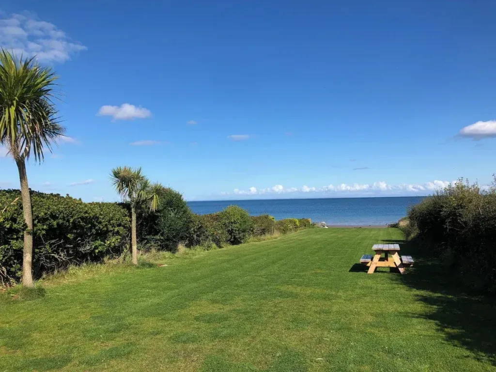 Long lawned garden with a picnic table and established planting leading towards the sea at Seal Bay Cottage