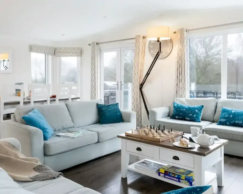 Shorefield Country Park, Milford-on-Sea, Hampshire 2 Bright living area with pale sofas, blue cushions, a chessboard on a coffee table and a dining area behind