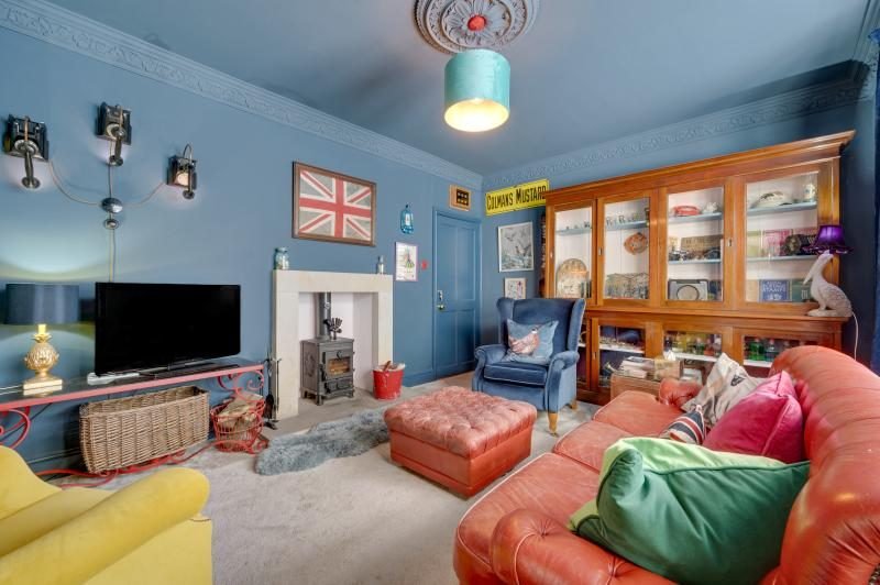 Colourful Cinema House near Craster, Northumberland 10 Blue-walled sitting room with a stove in a stone fireplace, leather sofa and glazed display cabinet