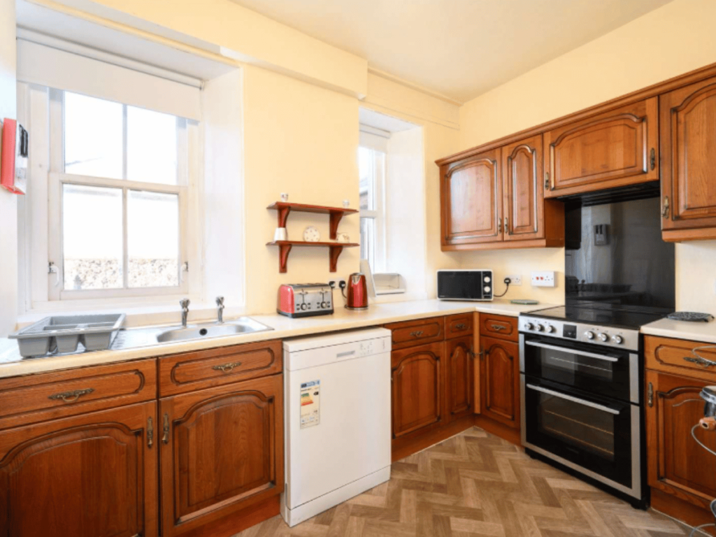Fitted kitchen at The Beacon in St Abbs with wooden cabinets, electric cooker, dishwasher and large windows