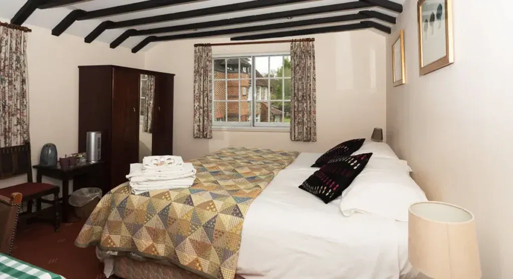 Bedroom at The Bull at Wargrave with exposed beams, patterned bed cover, wooden wardrobe and bedside lamp