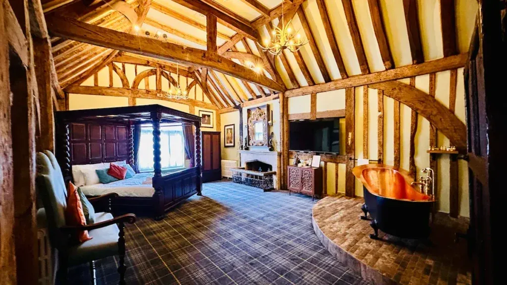 Timber-framed suite at The Ostrich Inn with a wooden four poster bed, copper-coloured roll-top bath and vaulted ceiling