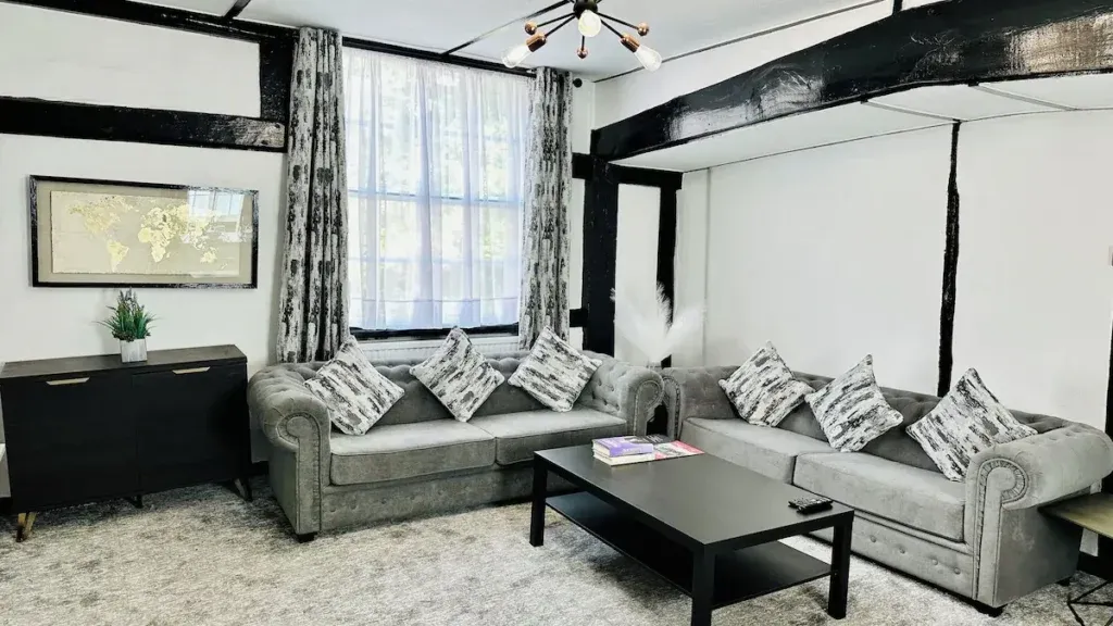 Lounge interior at The Ostrich Inn with two grey sofas, patterned cushions, a black coffee table and exposed dark beams