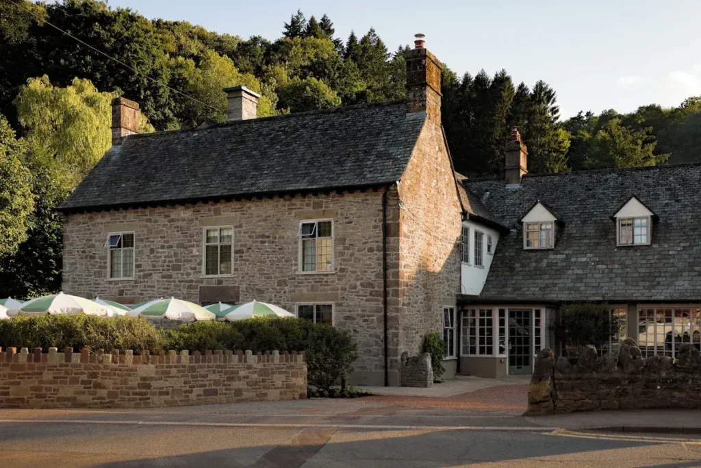 Historic stone exterior of The Royal George in Tintern with terrace umbrellas and wooded hills behind