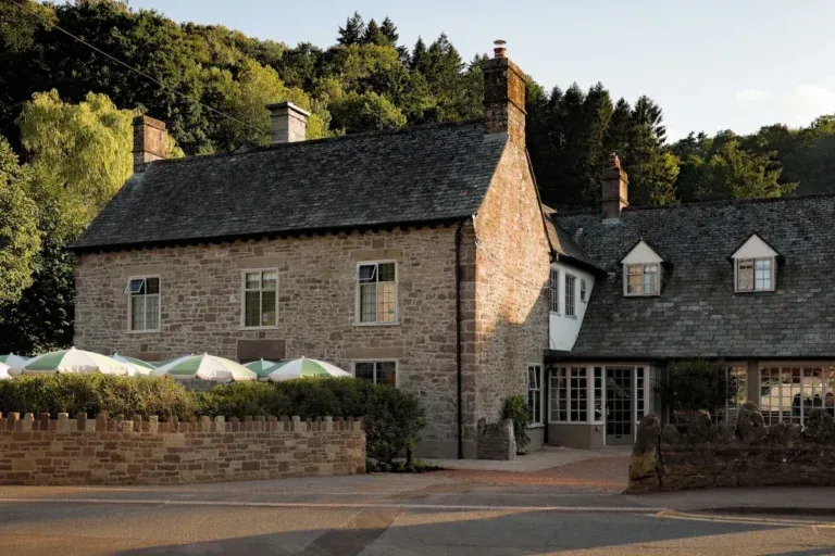 Historic stone exterior of The Royal George in Tintern with terrace umbrellas and wooded hills behind