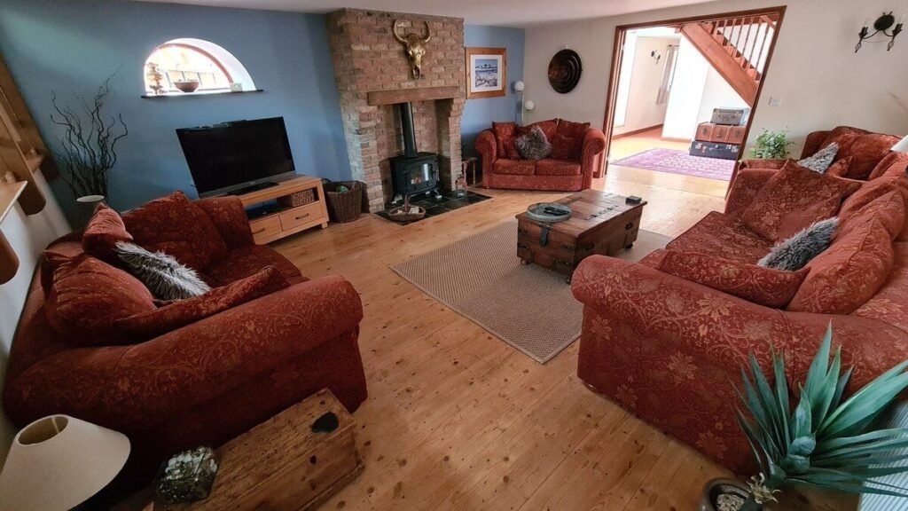 Wagtail Barn, South Devon 5 Living room at Wagtail Barn with red sofas, a television and a wood burner in a stone fireplace