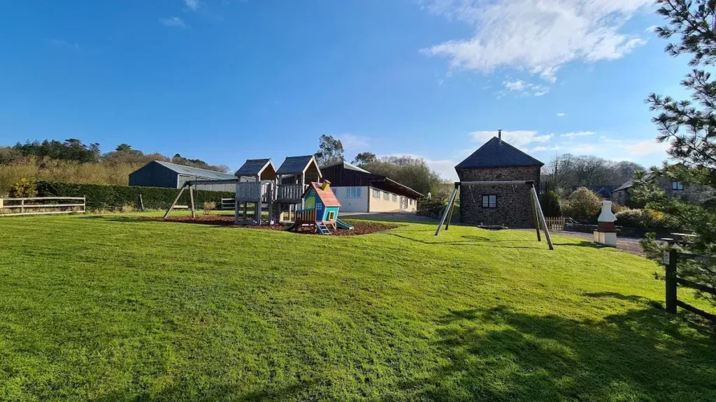 Wagtail Barn, South Devon 10 Large lawn with trees, play equipment and the barn beneath a sunset sky